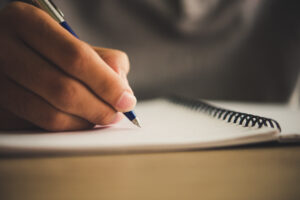 Une main écrivant avec un stylo bleu sur un cahier blanc à spirale.